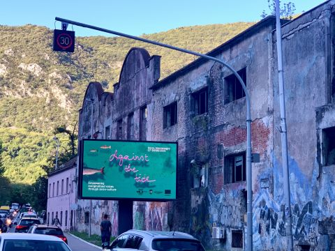 Plakat mit Ankündigung der ENCC Konferenz "Against the Tide" vor einem verfallenen Fabriksgebäude  – September 2025, Kotor / Montenegro,